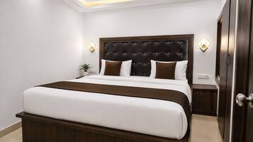 A neatly made bed with a dark headboard and white bedding, a bedside table with a lamp, and a door to the right.