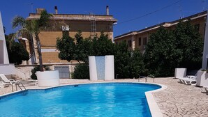 Une piscine rectangulaire à l’eau d’un bleu cristallin, entourée d’une terrasse en pierre et de chaises longues blanches.
