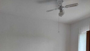 Une chambre à coucher avec un lit, deux tables de chevet, un ventilateur de plafond et une fenêtre avec des rideaux.
