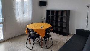 Une pièce comprenant une table à manger, des chaises, un téléviseur, une étagère noire et un lampadaire.