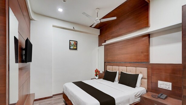A modern hotel room with a large bed, a ceiling fan, a bedside table with a phone, and a wall-mounted TV.