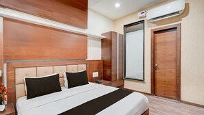 A hotel room with a large bed, wooden headboard, a wardrobe, a mirror, and an air conditioning unit.