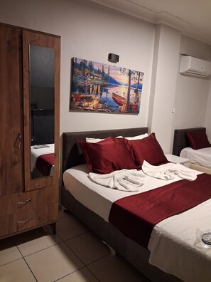 A hotel room with a bed, a wooden wardrobe, a painting of a lakeside scene, and an air conditioning unit.