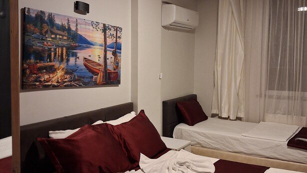 A hotel room with two beds, a painting on the wall, an air conditioning unit, and a window with sheer curtains.