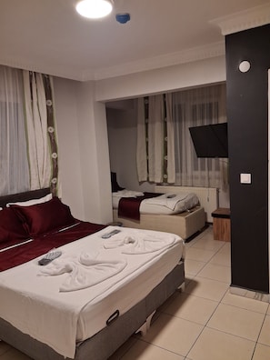 A hotel room with two beds, a TV, a small table, and a window with curtains. - Yağmur pansiyon (Istanbul)