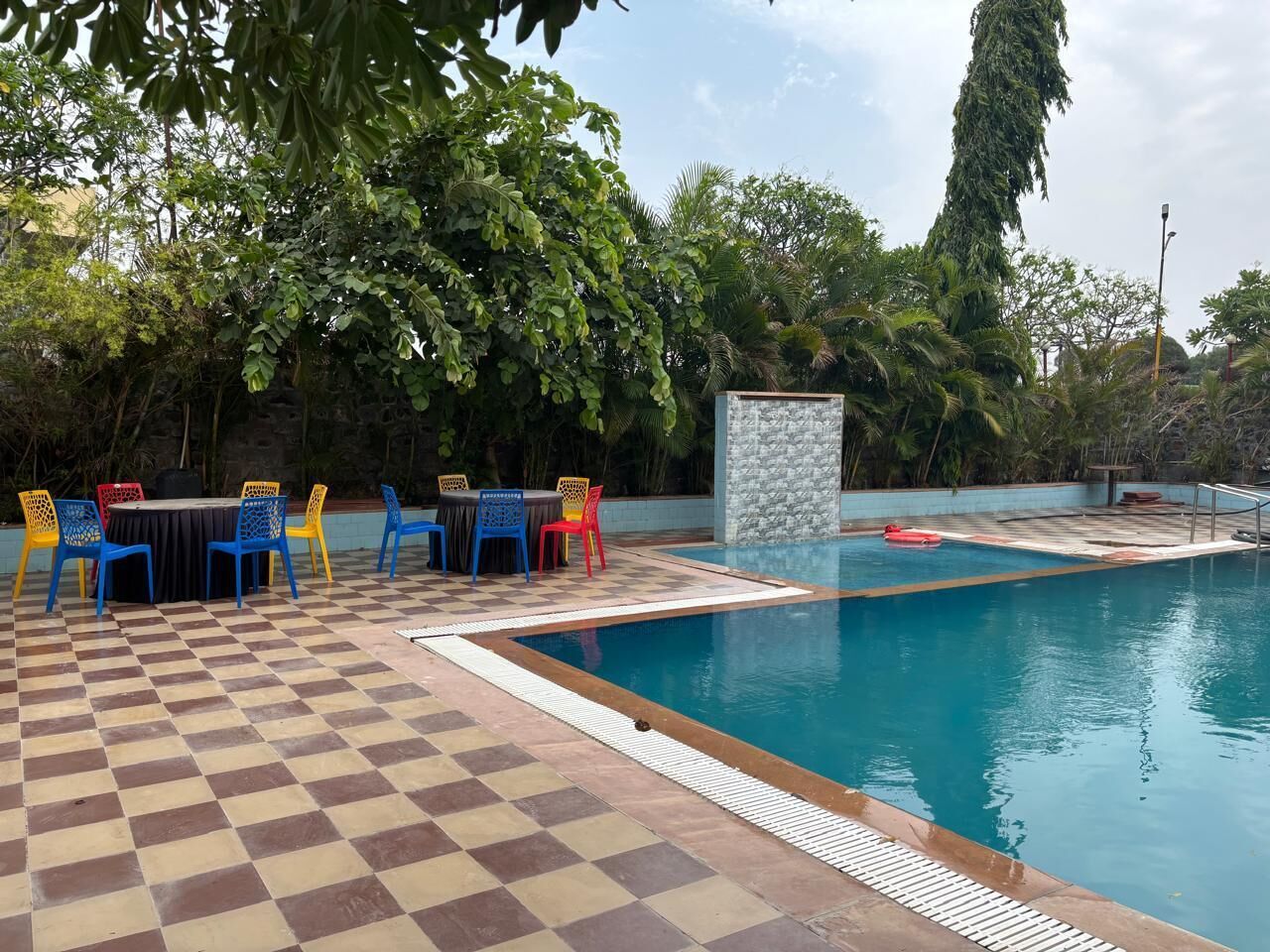 A swimming pool with checkered flooring, surrounded by trees and a stone wall.