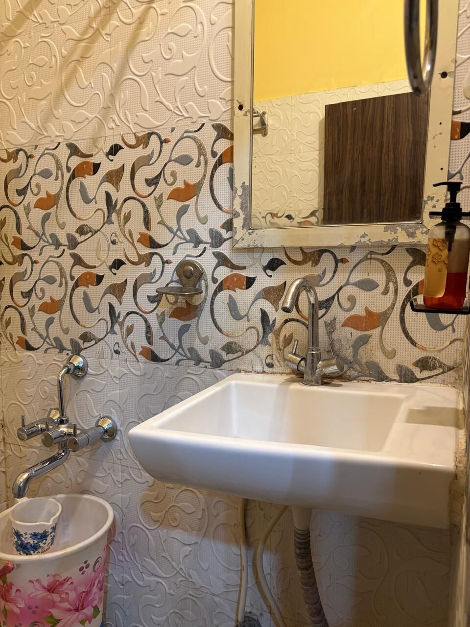A bathroom with a white sink, a mirror, and a patterned wall.
