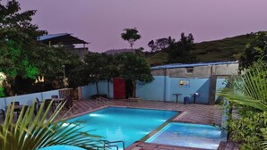 Una piscina con suelo a cuadros, rodeada de follaje y un edificio con techo azul.