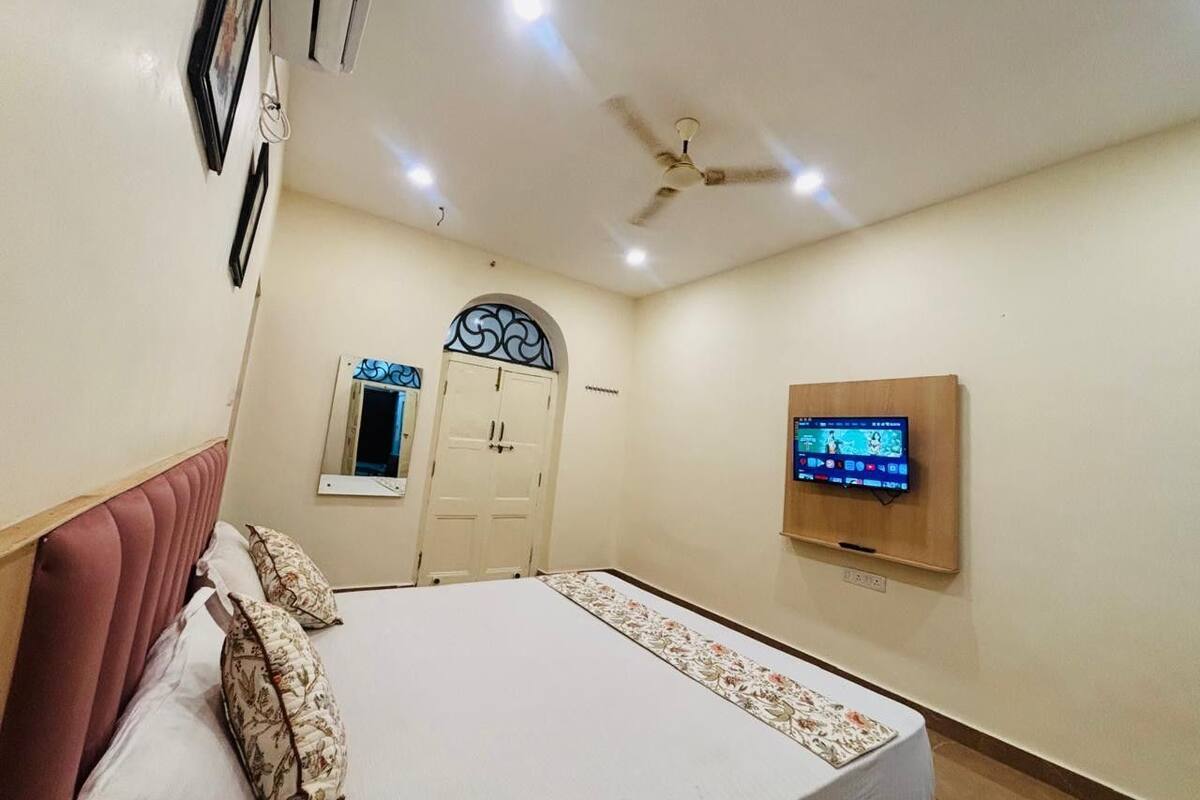 Ein Schlafzimmer mit einem Bett, einem Deckenventilator, einem an der Wand montierten Fernseher und einer Tür mit dekorativem Bogen.