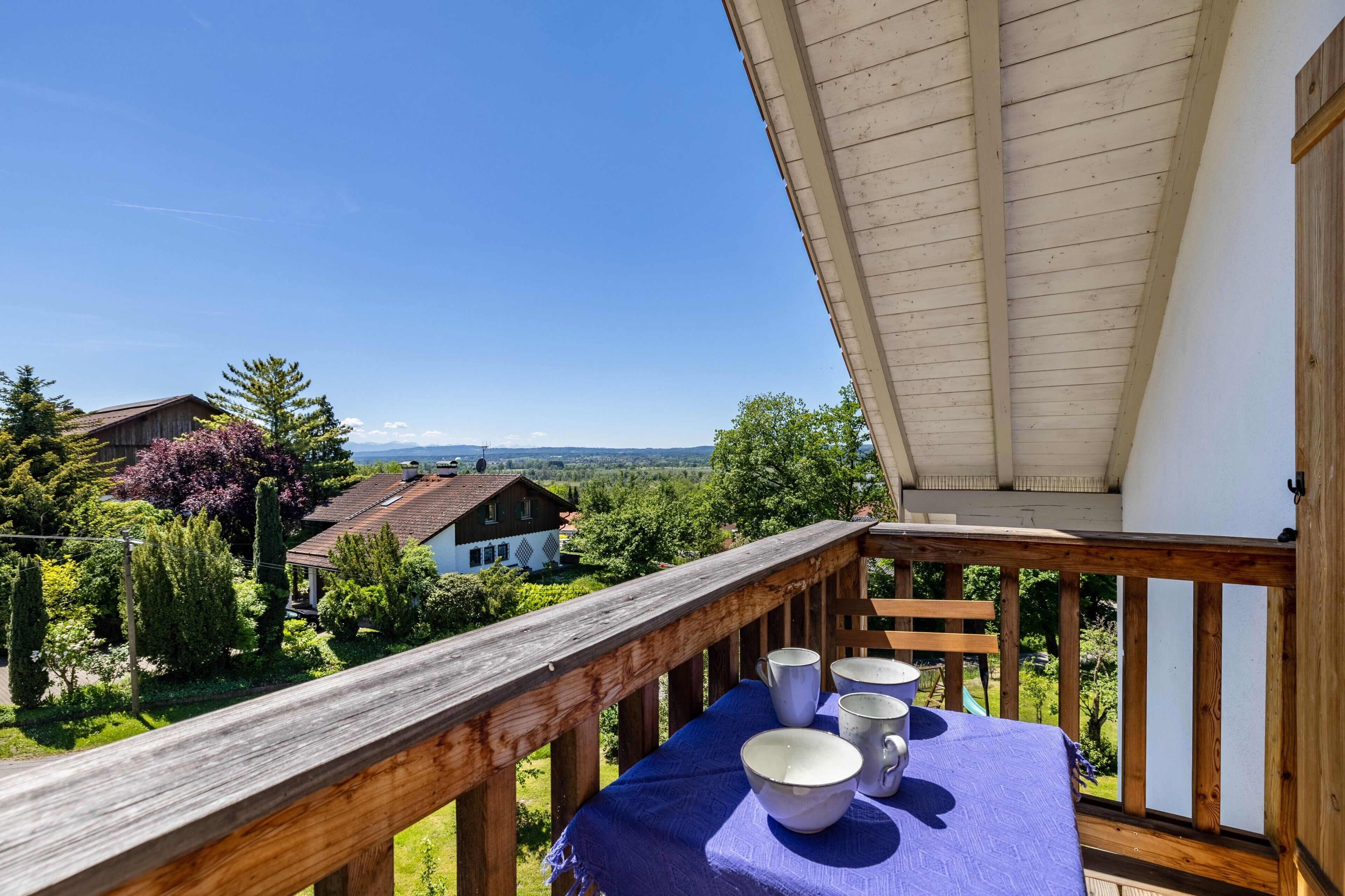 A balcony with a table set for four, overlooking a scenic landscape with houses and trees.