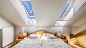 A bedroom with a skylight, a bed with floral bedding, two bedside tables with lamps, and a wooden headboard.