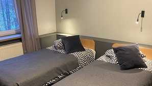 Ett rum med två sängar, ett fönster med gardiner, en vägglampa och ett element.