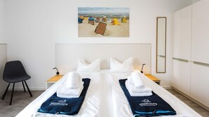 A hotel room with a bed, two nightstands, a chair, a painting of a beach, and a wardrobe. - MEERholung Vacation Rental 1.7: Close to the Beach, with Two Bedrooms and a Sofa Bed - House (Cuxhaven)