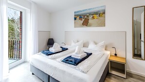 A hotel room with a large bed, a painting of beach huts, a chair, and a nightstand. - MEERholung Vacation Rental 1.7: Close to the Beach, with Two Bedrooms and a Sofa Bed - House (Cuxhaven)
