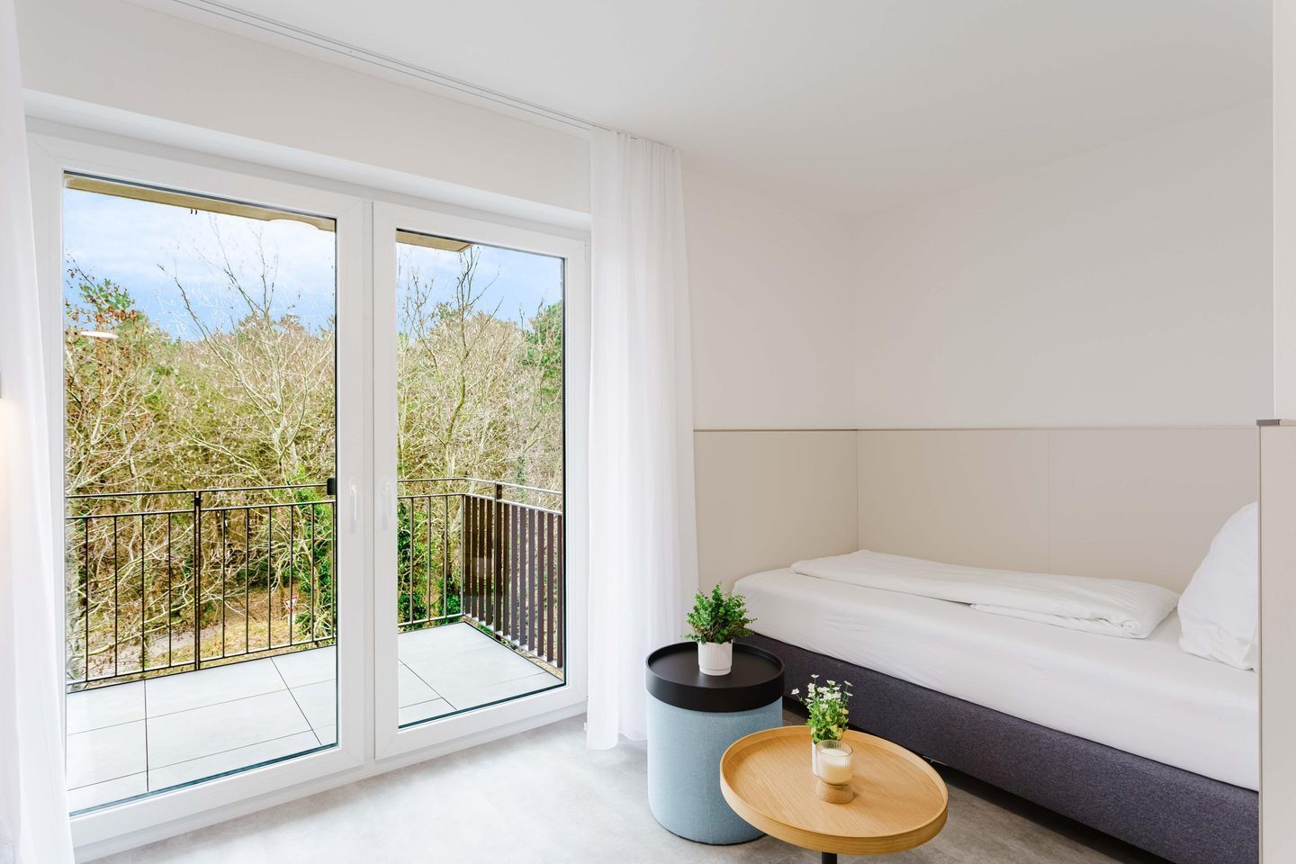 Une chambre moderne avec un lit, une petite table ronde agrémentée d’une plante, et un balcon doté d’une balustrade.