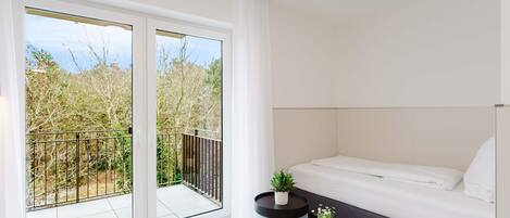 A modern room with a bed, a small round table with a plant, and a balcony with a railing.