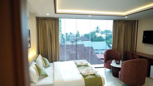 A hotel room with a bed, two chairs, a small table, and a TV. - Hotel Calicut Beach Annex (Kozhikode)