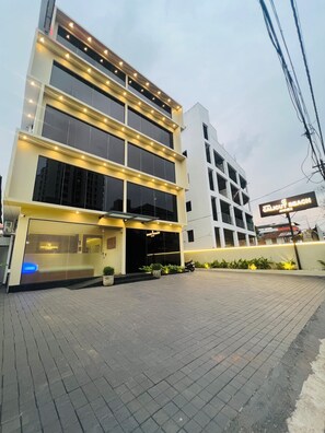 Un edificio moderno de varios pisos, con amplias ventanas y un letrero que indica un hotel.