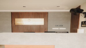 A reception desk with a modern design, a mounted screen displaying the hotel name, and a sign indicating the reception area. - Hotel Calicut Beach Annex (Kozhikode)