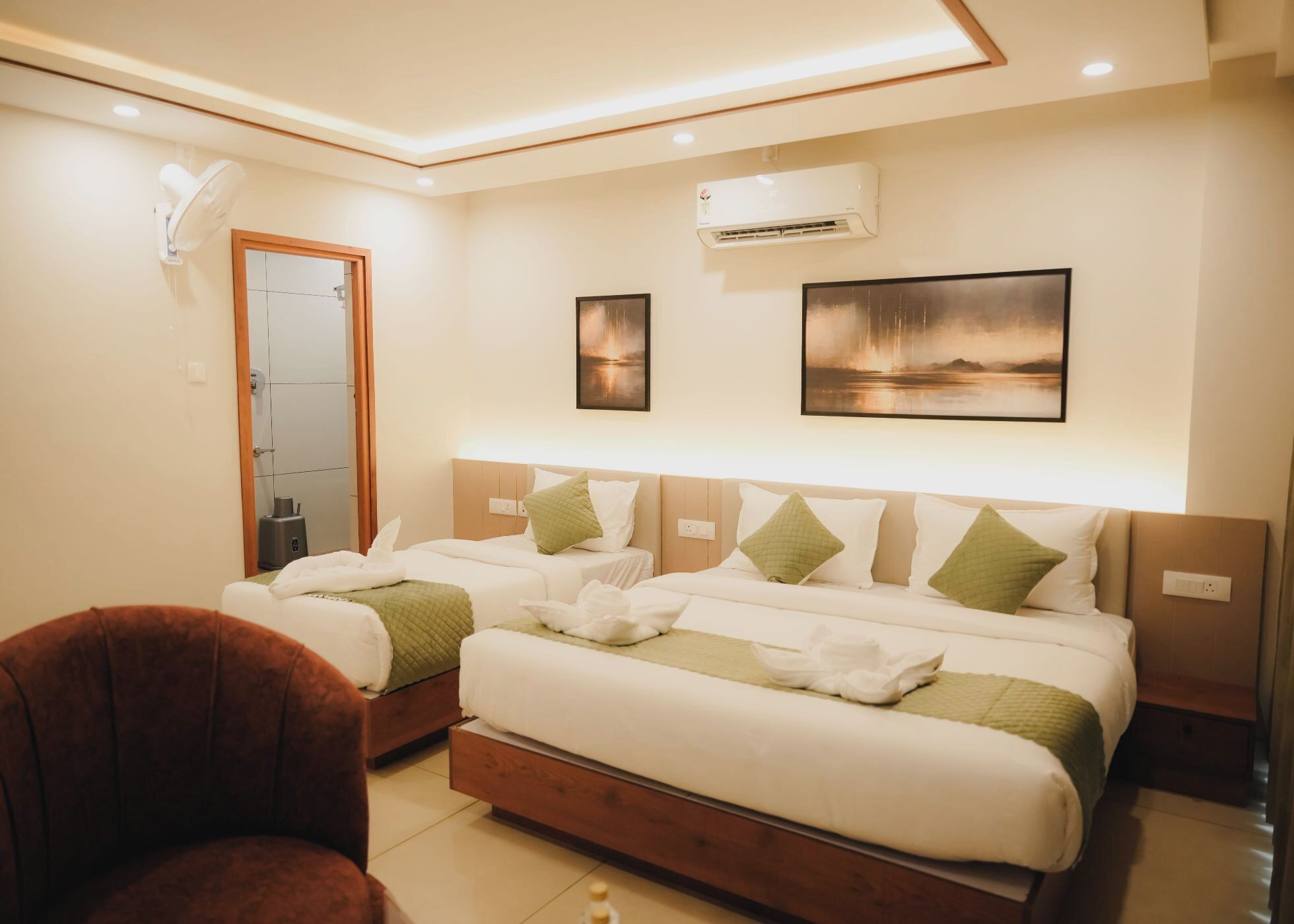 A hotel room with a large bed, two bedside tables, a chair, an air conditioning unit, and two framed pictures on the wall.