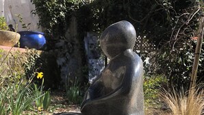 A sculpture of a seated figure on a stone pedestal surrounded by pebbles. - Quiet artist's house with stunning lake view. (Tresserve)
