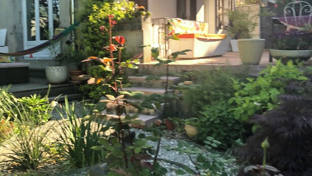 A residential building with a balcony, potted plants, and a garden area with various plants and a small table. - Quiet artist's house with stunning lake view. (Tresserve)