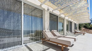 A modern outdoor lounge area with sunbeds and a glass wall. - Villa Mia Rose Ammoussa Lefkada (Lefkada)