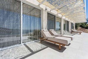 A modern outdoor lounge area with sunbeds and a glass wall. - Villa Mia Rose Ammoussa Lefkada (Lefkada)