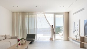 A modern living room with a sofa, a coffee table with a vase and flowers, a chair, and a large window with a view of the outdoors. - Villa Mia Rose Ammoussa Lefkada (Lefkada)