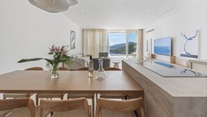 A modern dining area with a wooden table, wicker chairs, a vase with flowers, and a view of the sea through large windows. - Villa Mia Rose Ammoussa Lefkada (Lefkada)