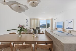 A modern dining area with a wooden table, wicker chairs, a vase with flowers, and a view of the sea through large windows. - Villa Mia Rose Ammoussa Lefkada (Lefkada)
