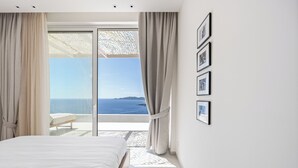 A bedroom with a large bed, a view of the sea, and a balcony with a chair. - Villa Mia Rose Ammoussa Lefkada (Lefkada)