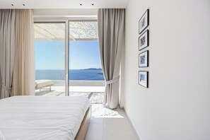 A bedroom with a large bed, a view of the sea, and a balcony with a chair. - Villa Mia Rose Ammoussa Lefkada (Lefkada)