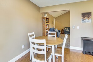 Un coin repas avec une table ronde et des chaises blanches, une bibliothèque et une poubelle.