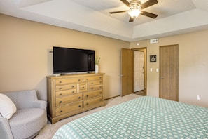 A bedroom with a bed, a dresser, a television, and a ceiling fan.