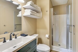 A bathroom with a white sink, a mirror, a glass shower enclosure, and a towel rack with folded towels.