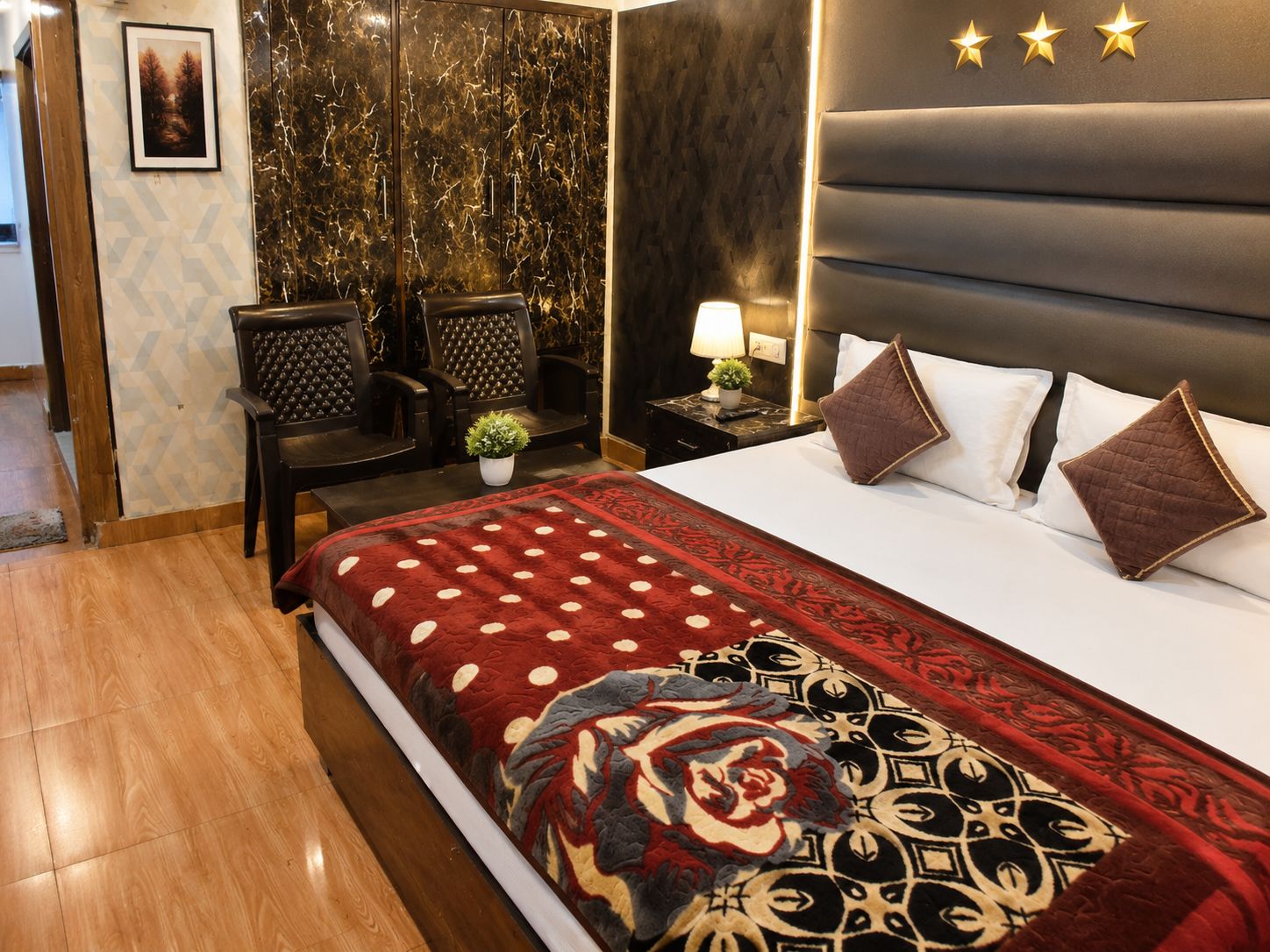 Una habitación de hotel con una cama, una mesita de noche, una lámpara, una planta en maceta y dos sillas.