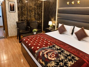 A hotel room with a bed, a nightstand, a lamp, a potted plant, and two chairs.