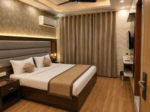 Habitación de hotel con cama, mesita de noche, cortinas, aire acondicionado y televisor.