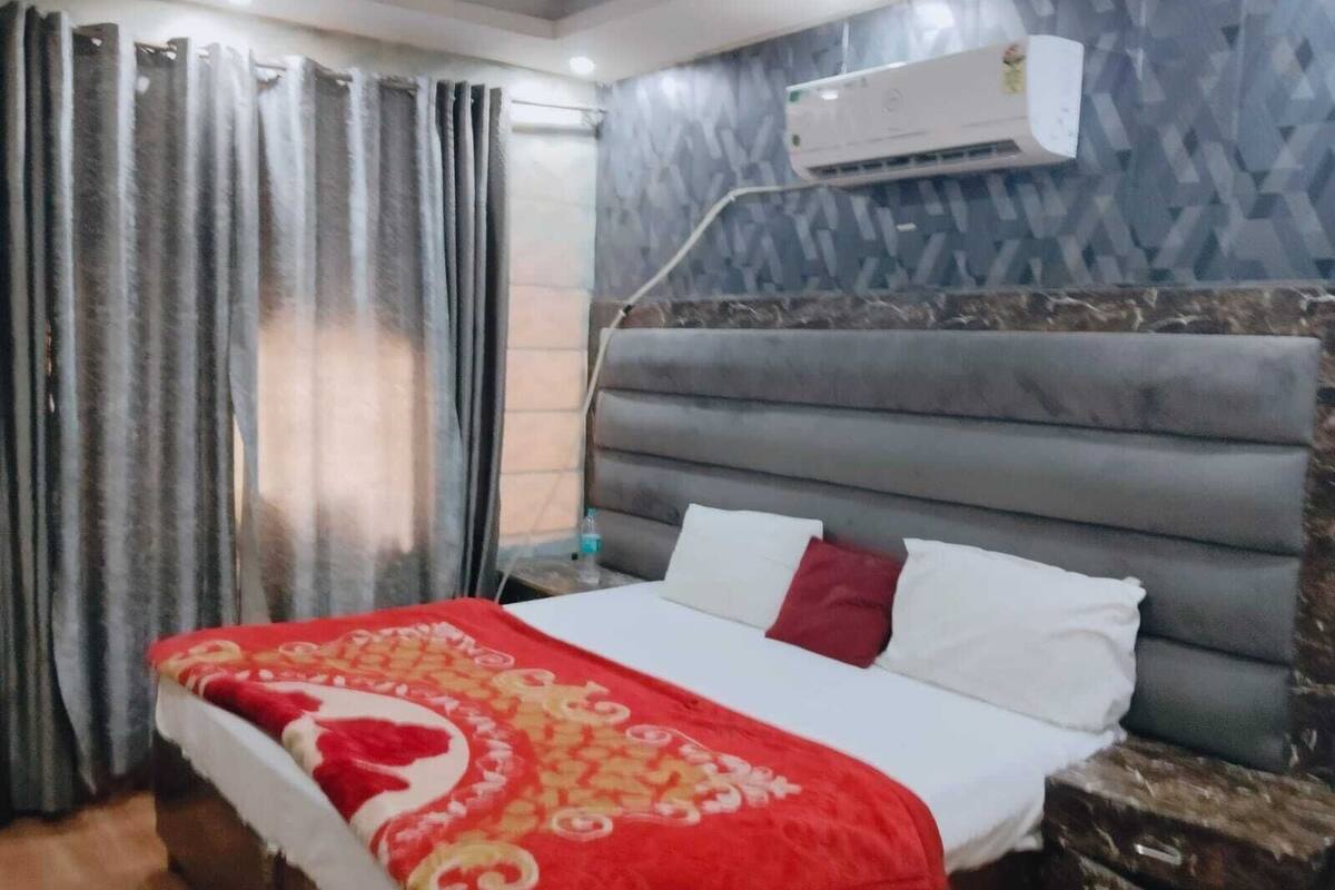 A hotel room with a bed, curtains, an air conditioning unit, and a patterned wall.
