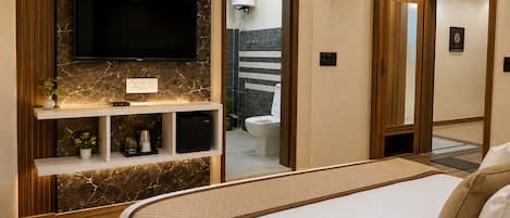 A modern bedroom with a large bed, a mounted TV, a shelf with decorative items, and a bathroom visible through an open door.