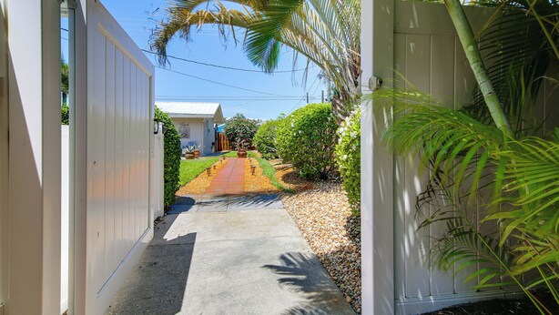 A gated pathway leading to a house with a well-maintained lawn and a clear sky. - 1 Mi to Vanderbilt Beach! Walkable Couple’s Haven (Naples)