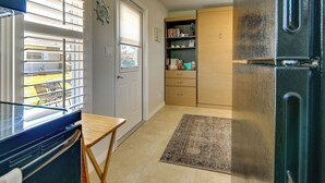 A compact kitchen with a refrigerator, a wooden cabinet, a small table, and a window with blinds. - 1 Mi to Vanderbilt Beach! Walkable Couple’s Haven (Naples)