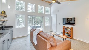 Un salon moderne avec un canapé en cuir, un ventilateur de plafond en bois et un téléviseur fixé au mur.