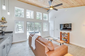 A modern living room with a leather sofa, a wooden ceiling fan, and a TV mounted on the wall. - Hike, Fish & Unwind: 2-Cabin Retreat in Hersey (Hersey)