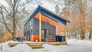 Une cabane moderne dotée d’une terrasse en bois, de grandes fenêtres et d’un espace extérieur aménagé et abrité.