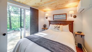 Une chambre avec un grand lit, un plafond en bois, deux lampes de chevet, une table de nuit et une vue sur une forêt, visible à travers une porte-fenêtre coulissante.