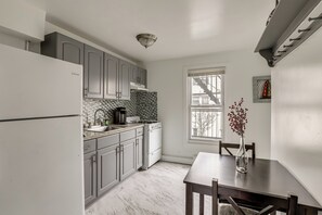 A kitchen with white cabinets, a marble floor, a dining table, and a window with a view.