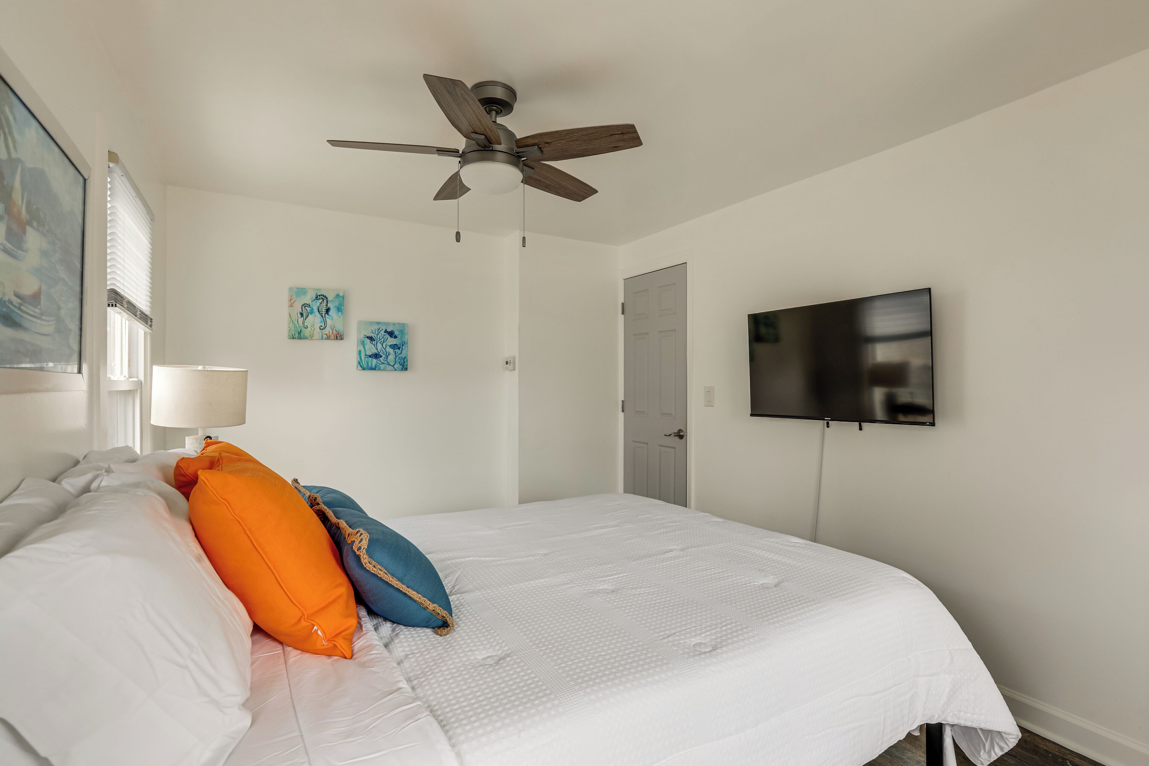 A bedroom with a bed, ceiling fan, wall-mounted TV, and artwork.
