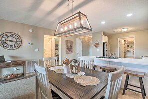 A dining area with a wooden table, white chairs, a chandelier, and a clock on the wall. - 2-Unit Escape - Pointe Royale Golf Resort, Pools (Branson)